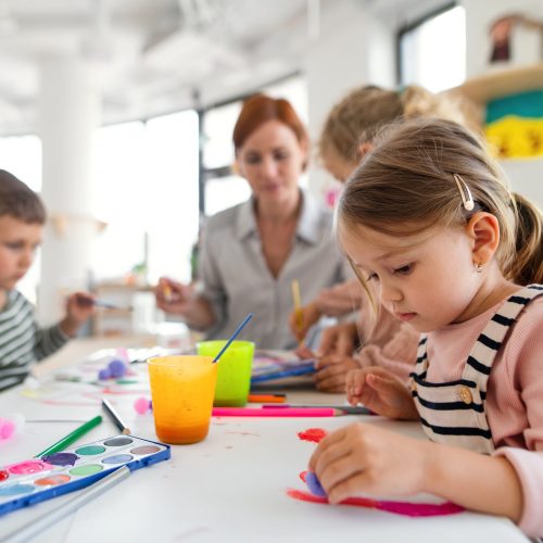 A group of small nursery school children with teacher indoors in classroom, painting.